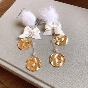 Close-up detail of elegant white fur ball earrings with ribbon bows and hammered gold discs