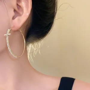 Close-up detail of a gold hoop earring featuring a sparkling rhinestone cross motif.