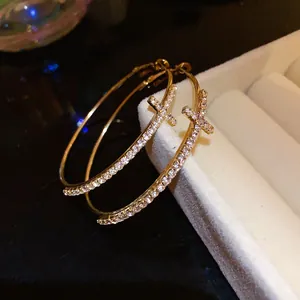 Detailed close-up of gold cross hoop earrings with sparkling stones on display tray