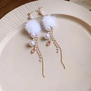 Detailed view of elegant earrings featuring white fur pom-poms, pearls and pink crystals