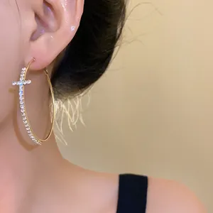 Close-up of gold-colored hoop earrings featuring a rhinestone-studded cross design
