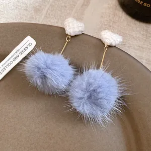 Detail of light blue pom pom earrings with white woven heart studs on a brown dish.