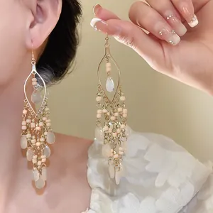 Close-up detail of bohemian teardrop earrings with peach beads and gold-tone hooks.