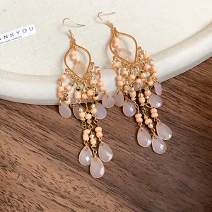 Close-up of bohemian earrings with pink acrylic teardrops and beads on wooden surface