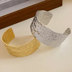 Close-up detail of textured hammered metal open cuff bracelets in gold and silver