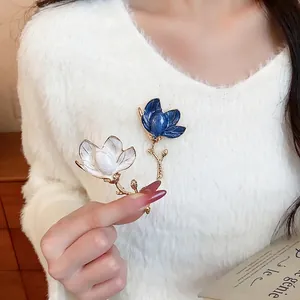 Elegant enamel flower brooch with gold-toned stem on white fuzzy sweater.