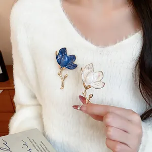 Close-up of elegant blue and white enamel flower brooches on a soft white sweater.
