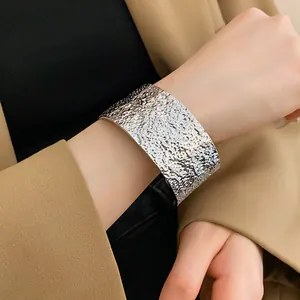 Macro detail of a silver-toned textured wide cuff bangle styled with a camel blazer.