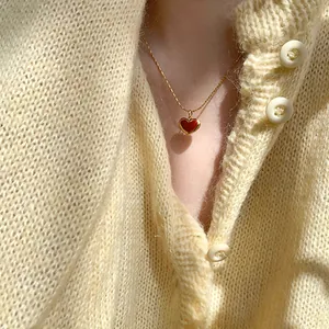 Élégant collier minimaliste en or avec pendentif cœur rouge sur pull en maille crème