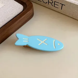 Detailed close-up of a cute light blue fish-shaped duckbill hair clip on a table surface