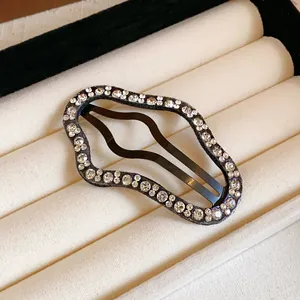 Detailed macro view of a sparkling rhinestone wave-shaped hair clip on a cream velvet tray