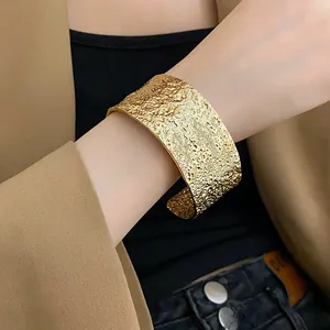 Detail showing the hammered texture of a wide gold cuff bracelet on a fashion model's wrist.
