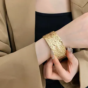 Macro view of a stylish wide gold-textured metal cuff bangle worn on a model's wrist