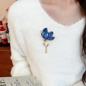 Detailed view of an elegant blue enamel flower brooch pinned on a white fuzzy sweater.