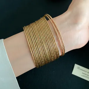 Macro-detail van meerdere goudkleurige metalen armbanden met textuur om de pols.