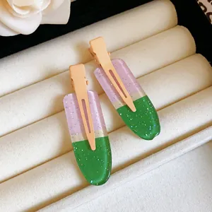 Close-up of glittery purple and green gradient duckbill hair clips on white velvet