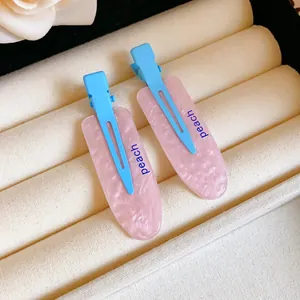 Close-up of pink and blue hair clips with peach lettering on a cream display tray.