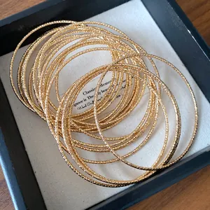 Detail van stapelbare gouden armbanden met elegante textuurpatronen in een luxe geschenkdoos