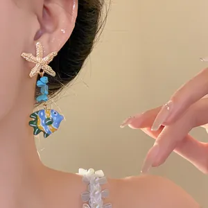 Close-up of golden starfish and colorful glass fish pendant earring being worn on an ear