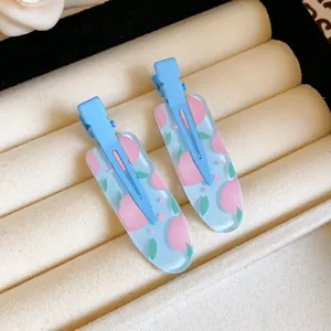 Close-up detail of light blue duckbill hair clips with pink fruit patterns on velvet