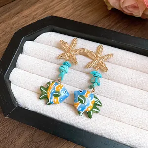 Close-up of beach-style earrings with starfish studs and glass fish pendants.