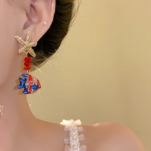 Detail view of the glazed fish and starfish earring worn on a model's ear.