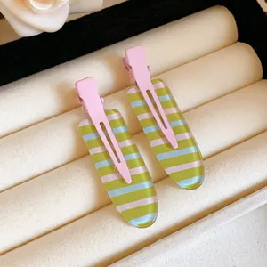Macro view of pastel striped acrylic duckbill hair clips displayed in a cream jewelry tray