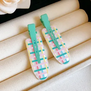 Close-up of mint green duckbill hair clips with colorful plaid pattern in a jewelry box