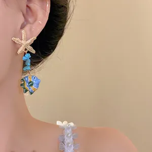 Close-up detail of starfish and colorful glass fish pendant stud earrings on ear