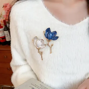 Detailed view of elegant white and blue enamel flower brooches on a white sweater