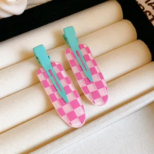 Macro view of two pink and white checkerboard duckbill hair clips with a glittery finish.