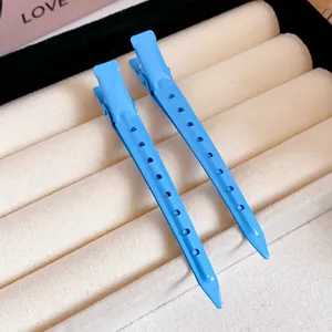 Close-up detail of two vibrant light blue duckbill hair clips on a beige jewelry display