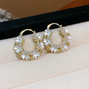 Primo piano di orecchini a cerchio placcati oro 14K con delicati petali bianchi.