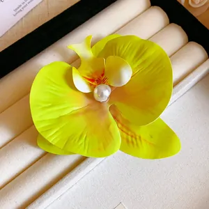 Detailed view of a vibrant yellow orchid flower hair clip with a central pearl embellishment
