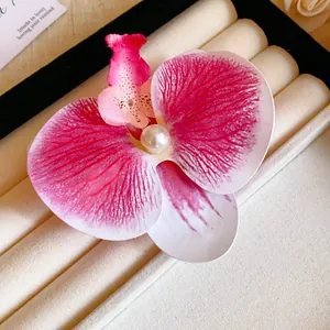 Close-up of a realistic pink orchid flower hair clip with a pearl center on a jewelry tray