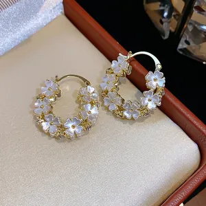 Primo piano di eleganti orecchini a cerchio placcati oro con delicati motivi floreali bianchi