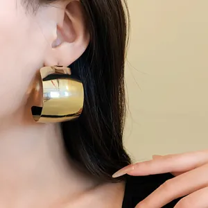 Primo piano dettagliato di audaci orecchini a cerchio dorati a forma di C indossati da modella