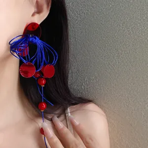 Close-up of Chinese style red and blue tassel earring on female model with long nails.