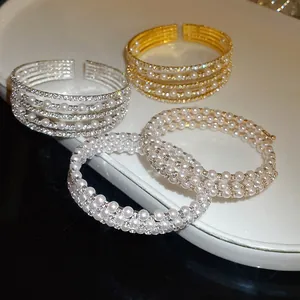 Close-up of layered open cuff bracelets with elegant pearls and sparkling rhinestones