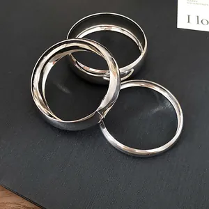Close-up detail of three stacked metallic geometric silver bangles with a smooth glossy finish