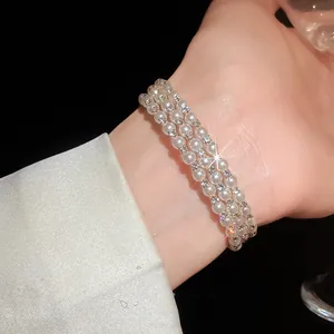 Elegant multi-layer pearl and rhinestone open bracelet worn on wrist with silk sleeve detail