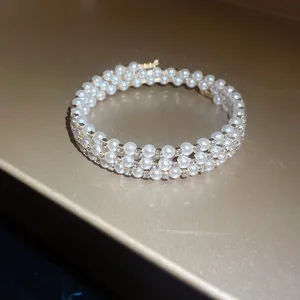 Close-up macro detail of three-layer gold bangle with white pearls and small rhinestones