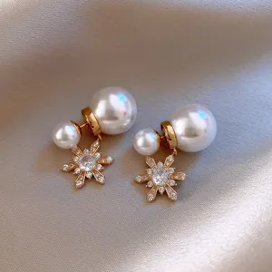 Close-up of elegant gold flower earrings with white pearls and sparkling cubic zirconia