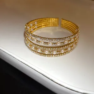 Macro view of a luxurious multi-layer gold open cuff bracelet with rhinestones and pearls.