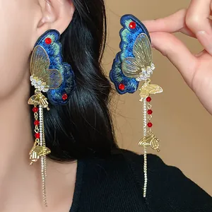 Detailed view of blue embroidered butterfly earrings with red rhinestones and tassels.
