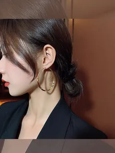 Close-up of large gold-toned metallic hoop earrings worn by a model for elegant style