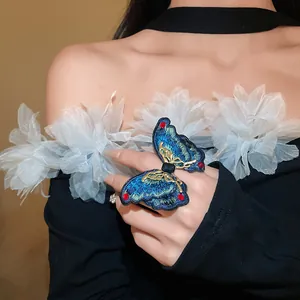 Detailed close-up of a large blue embroidered butterfly ring on a model's hand.