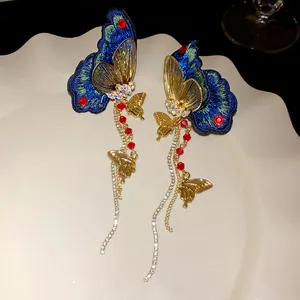 Macro detail of elegant embroidered butterfly earrings with long golden tassels and red beads