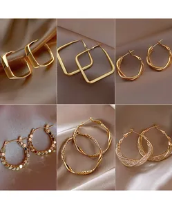 Selection of elegant gold-toned metal hoop and square earrings on satin fabric background