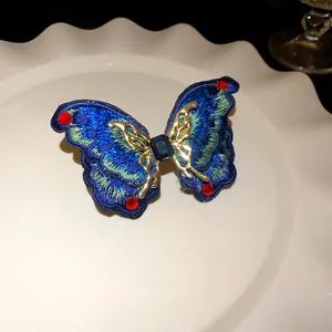 Macro detail of blue embroidered butterfly earring with gold frame and red stones